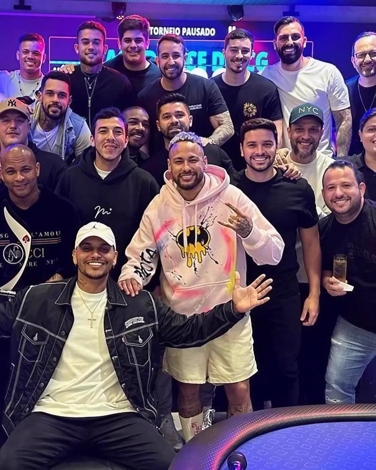 Neymar Jr vestindo um moletom pintado à mão por Gabriel Freire, em uma mesa de pôquer com outros convidados